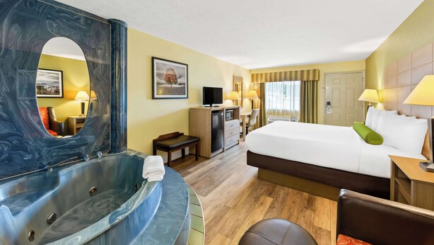 A hotel room with a large bed, a sitting area with a desk and chair, a television, a minibar, and a large mirror. - Best Western Dayton (Dayton)