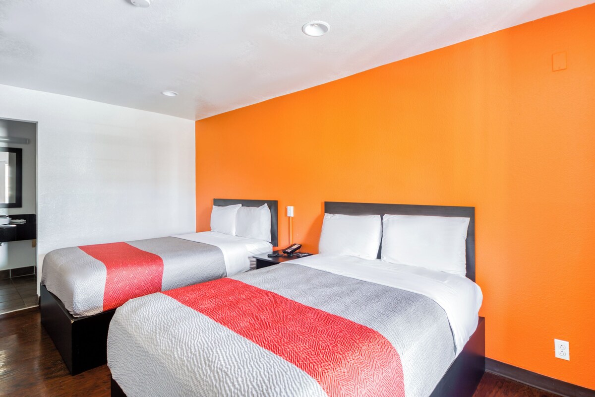 A hotel room with two beds, a nightstand, and an orange accent wall.