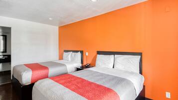 Habitación de hotel con dos camas, una mesita de noche y un baño visible al fondo.