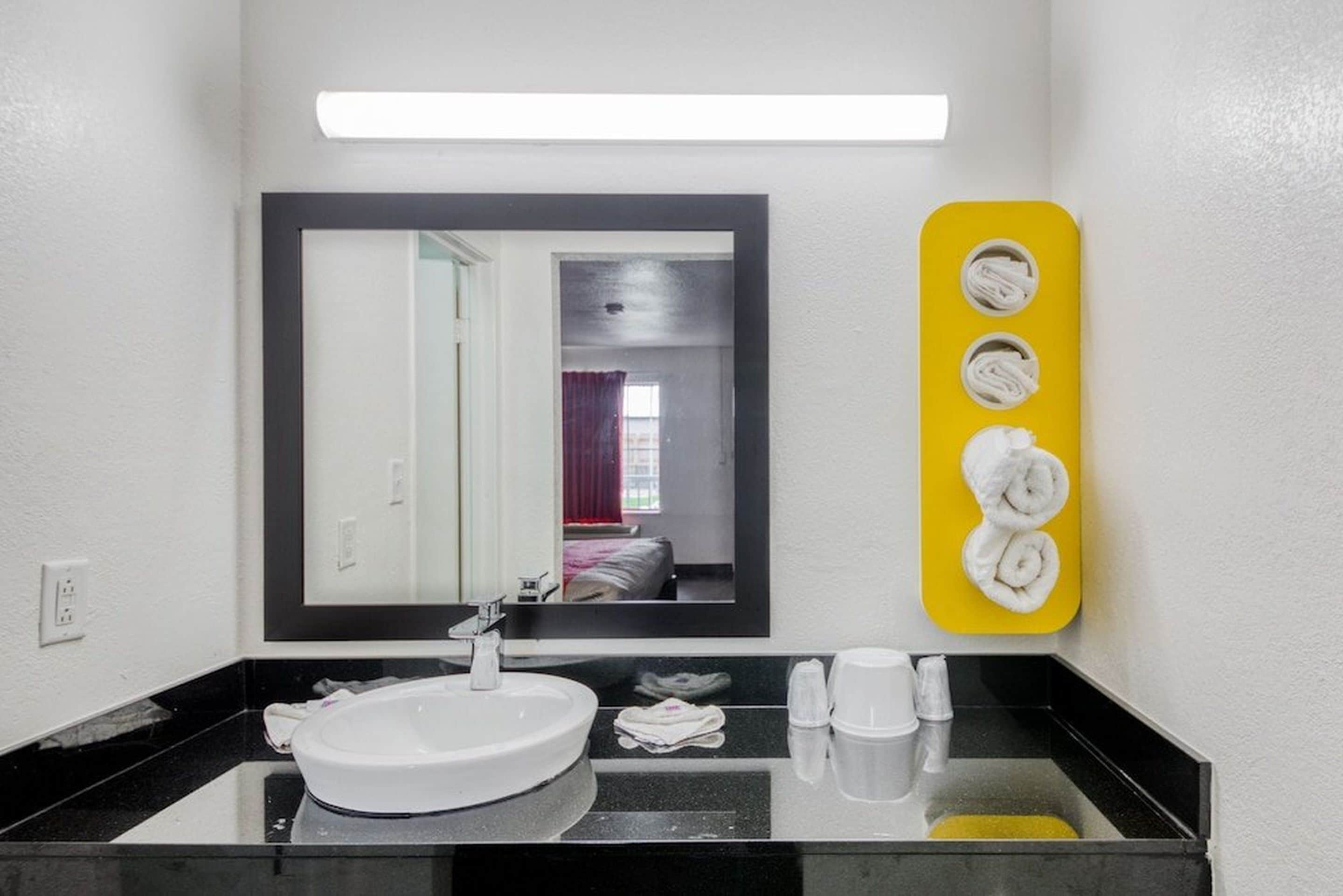 Een badkamer met een witte wastafel, een spiegel en een geel handdoekrek met handdoeken.