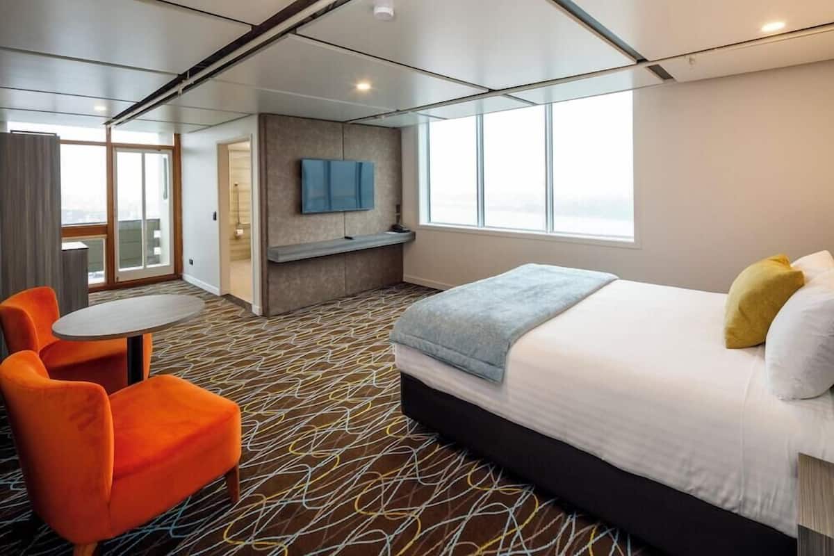 A hotel room with a bed, a TV, a seating area, and a window.