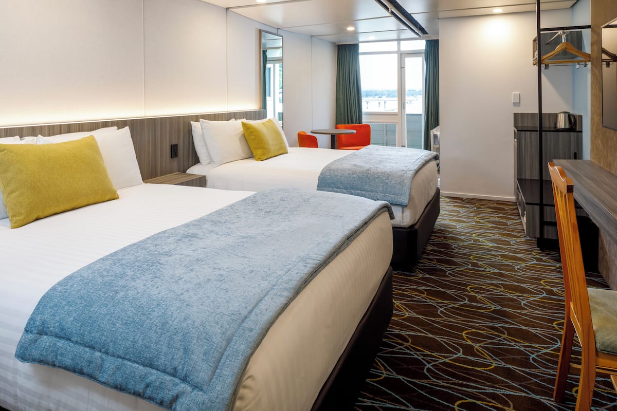 A hotel room with two beds, a small table, a chair, and a TV.