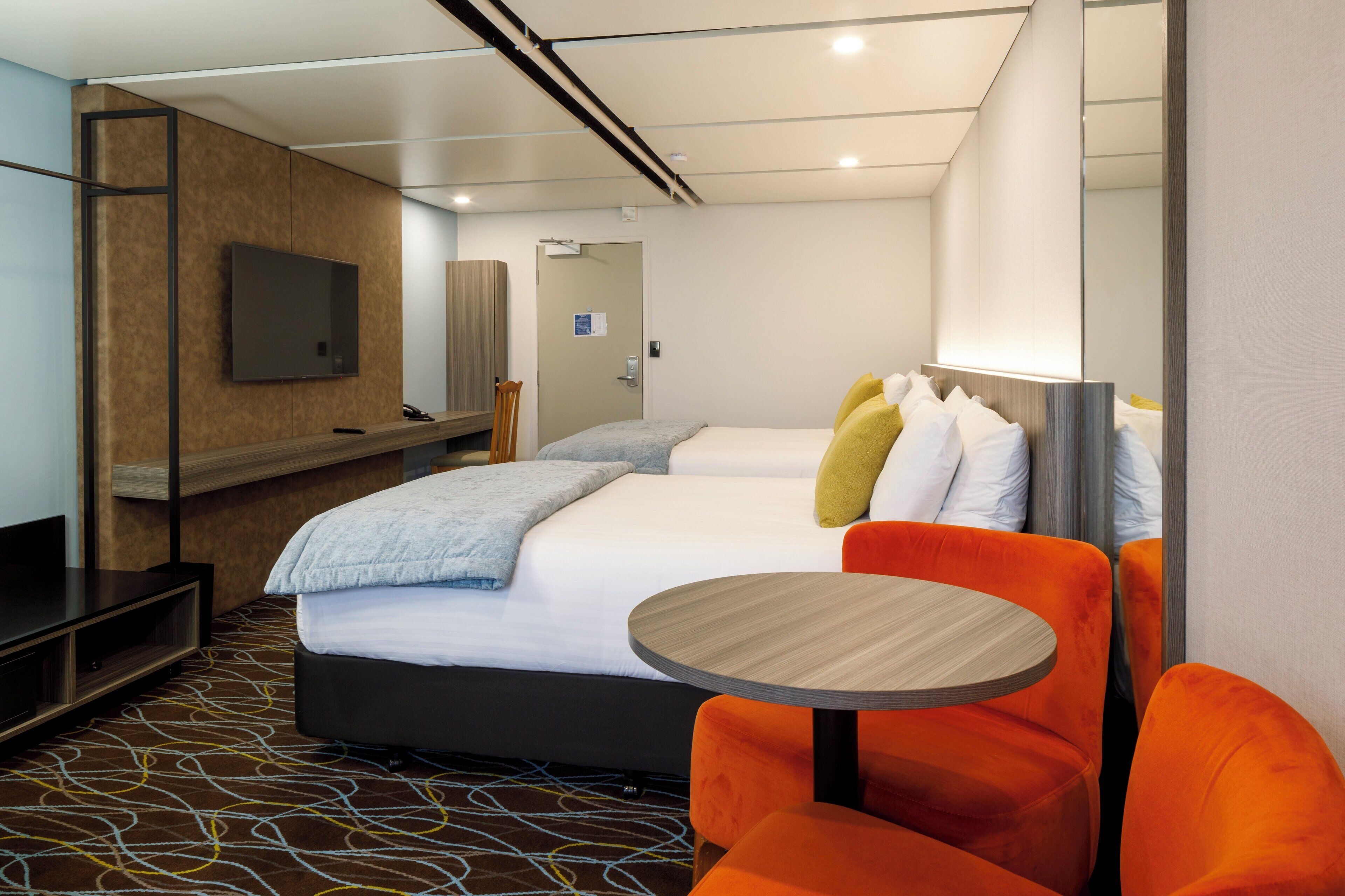 Una habitación de hotel moderna con una cama, un televisor, un escritorio y una mesa redonda.