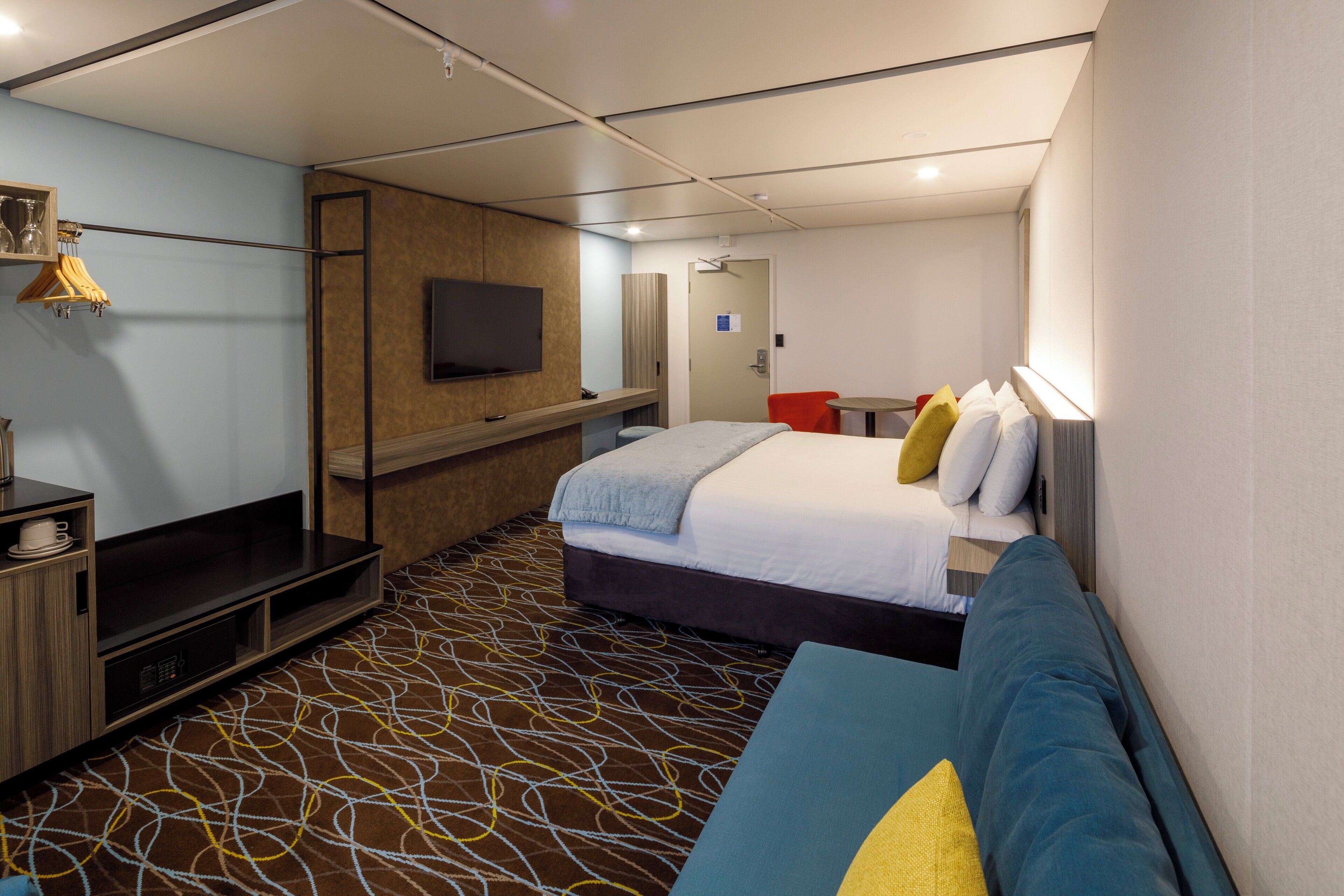 A hotel room with a bed, a sofa, a TV, a desk, and a patterned carpet.