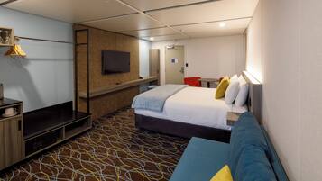 A hotel room with a bed, a sofa, a TV, a desk, and a patterned carpet.