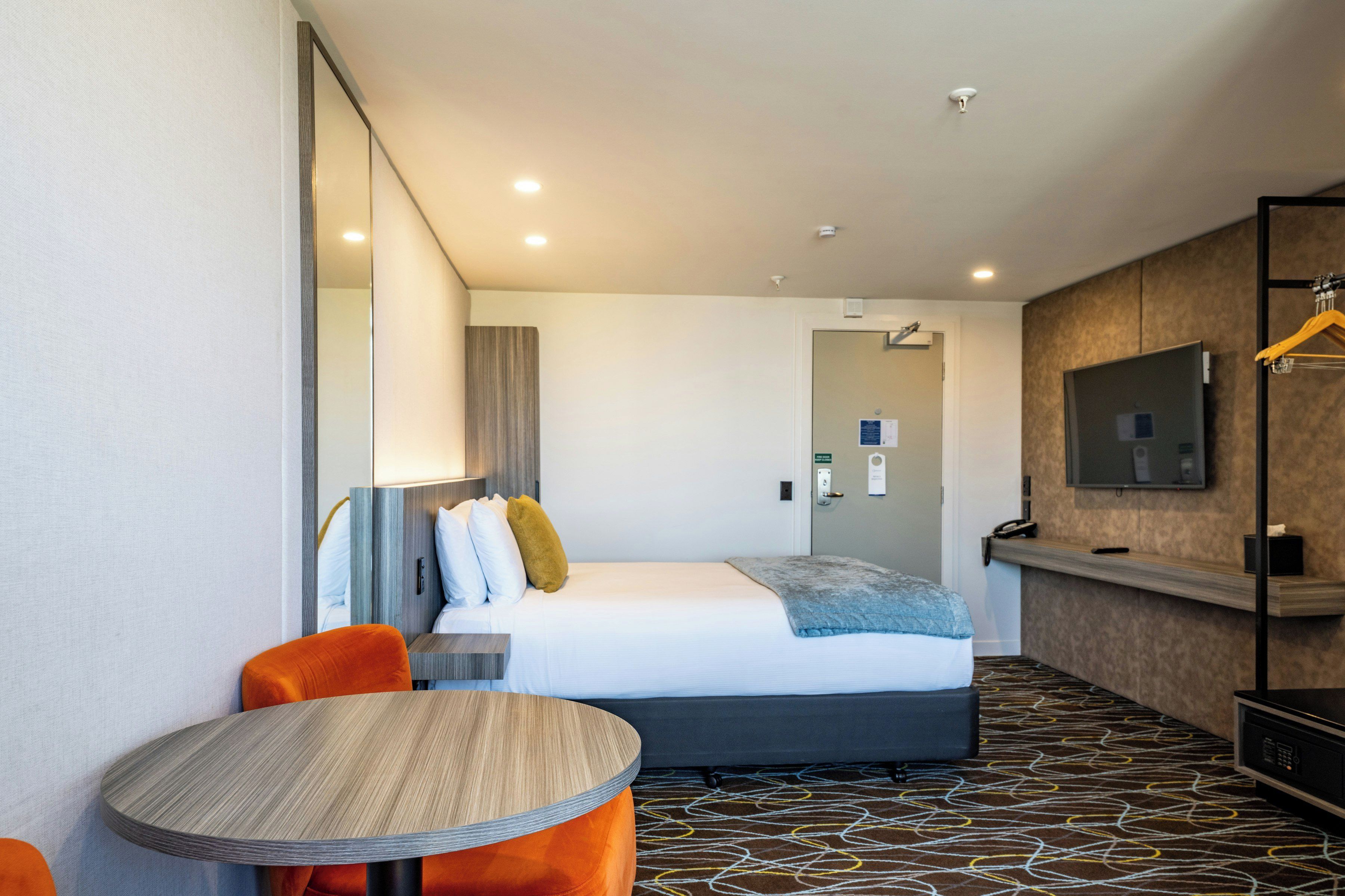 Una habitación de hotel con una cama, una mesa redonda, un televisor y un espejo.
