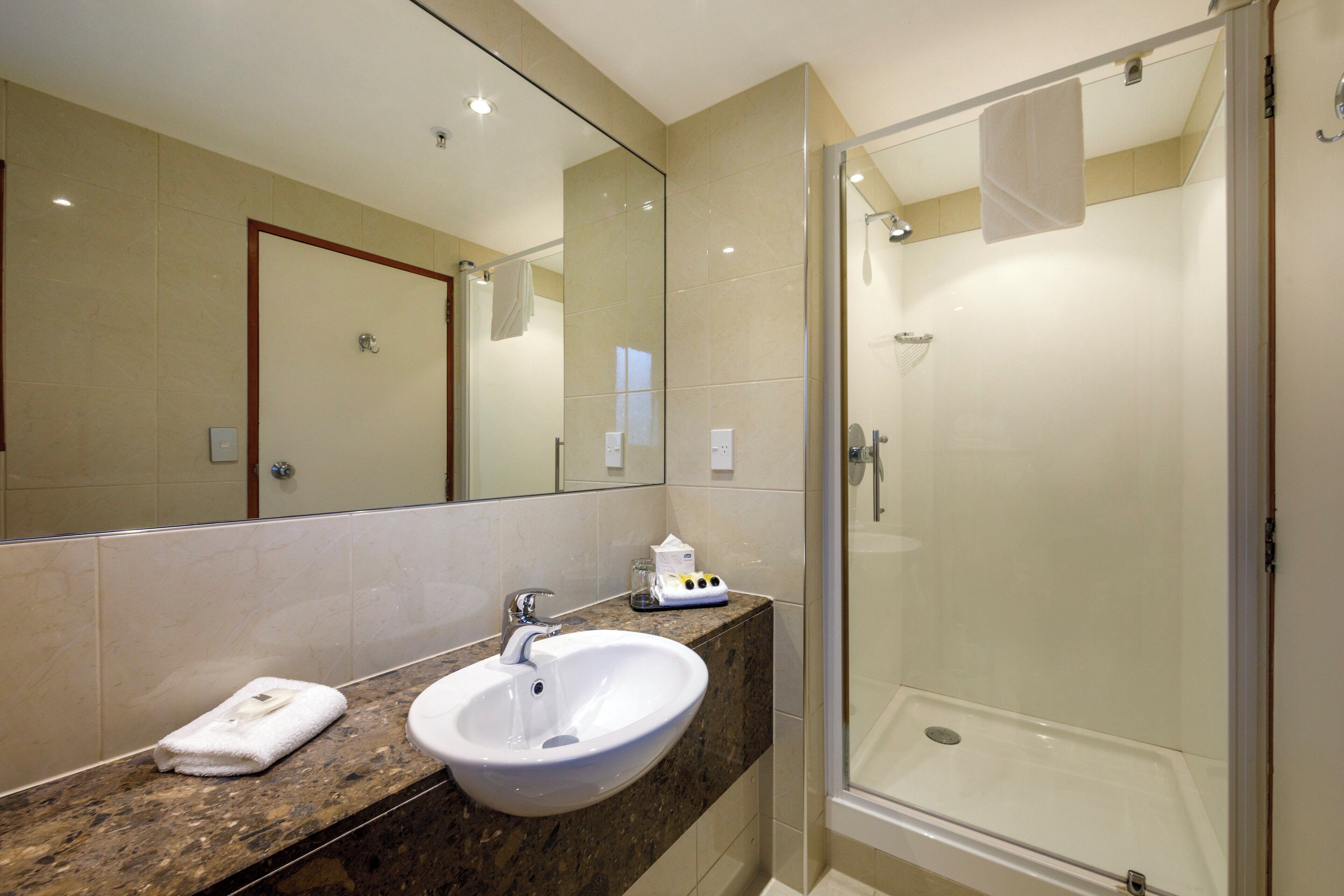 A bathroom with a marble countertop, a white sink, a glass shower enclosure, and a large mirror.