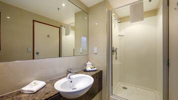 A bathroom with a marble countertop, a white sink, a glass shower enclosure, and a large mirror.