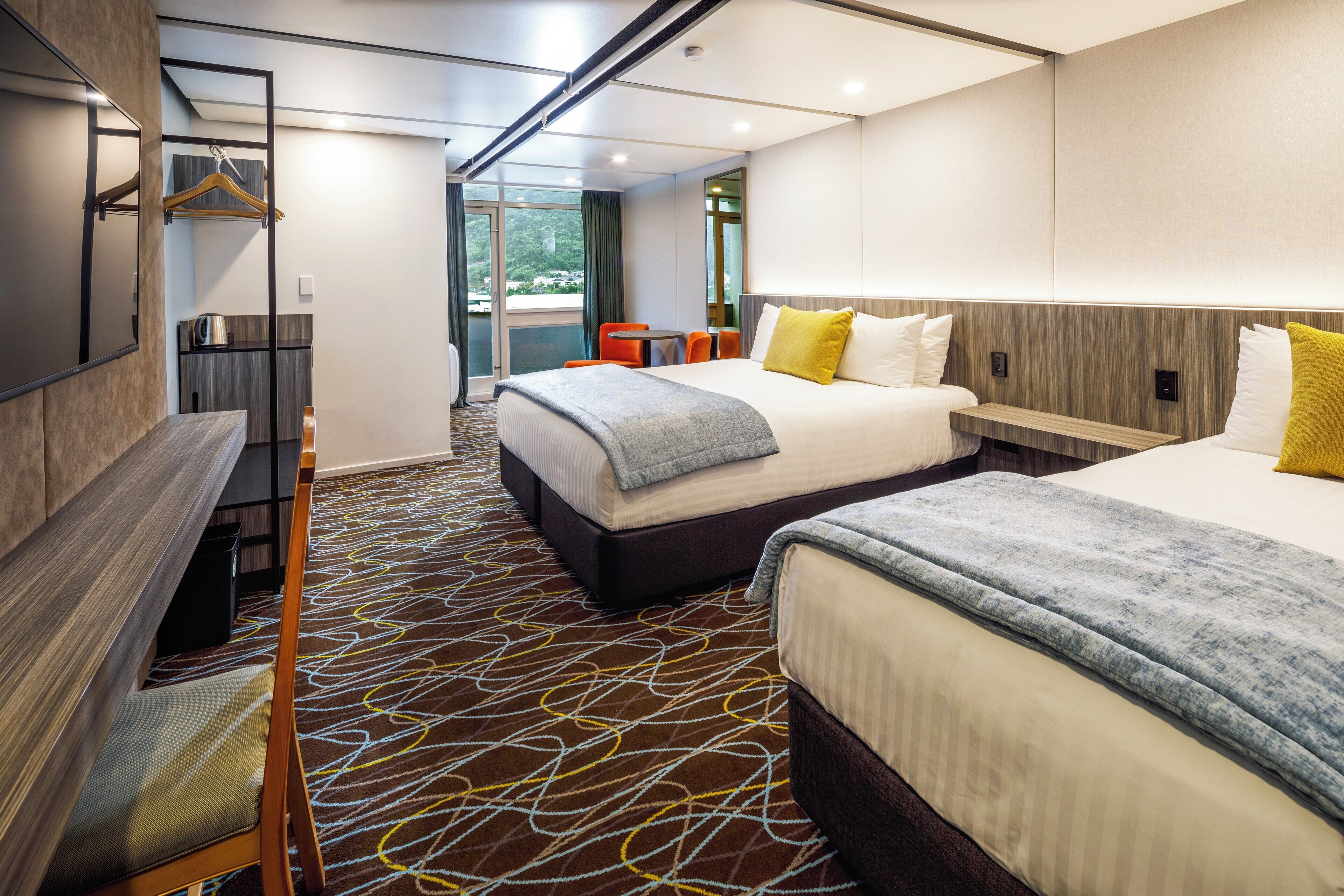 A hotel room with two beds, a desk, a chair, and a small table.