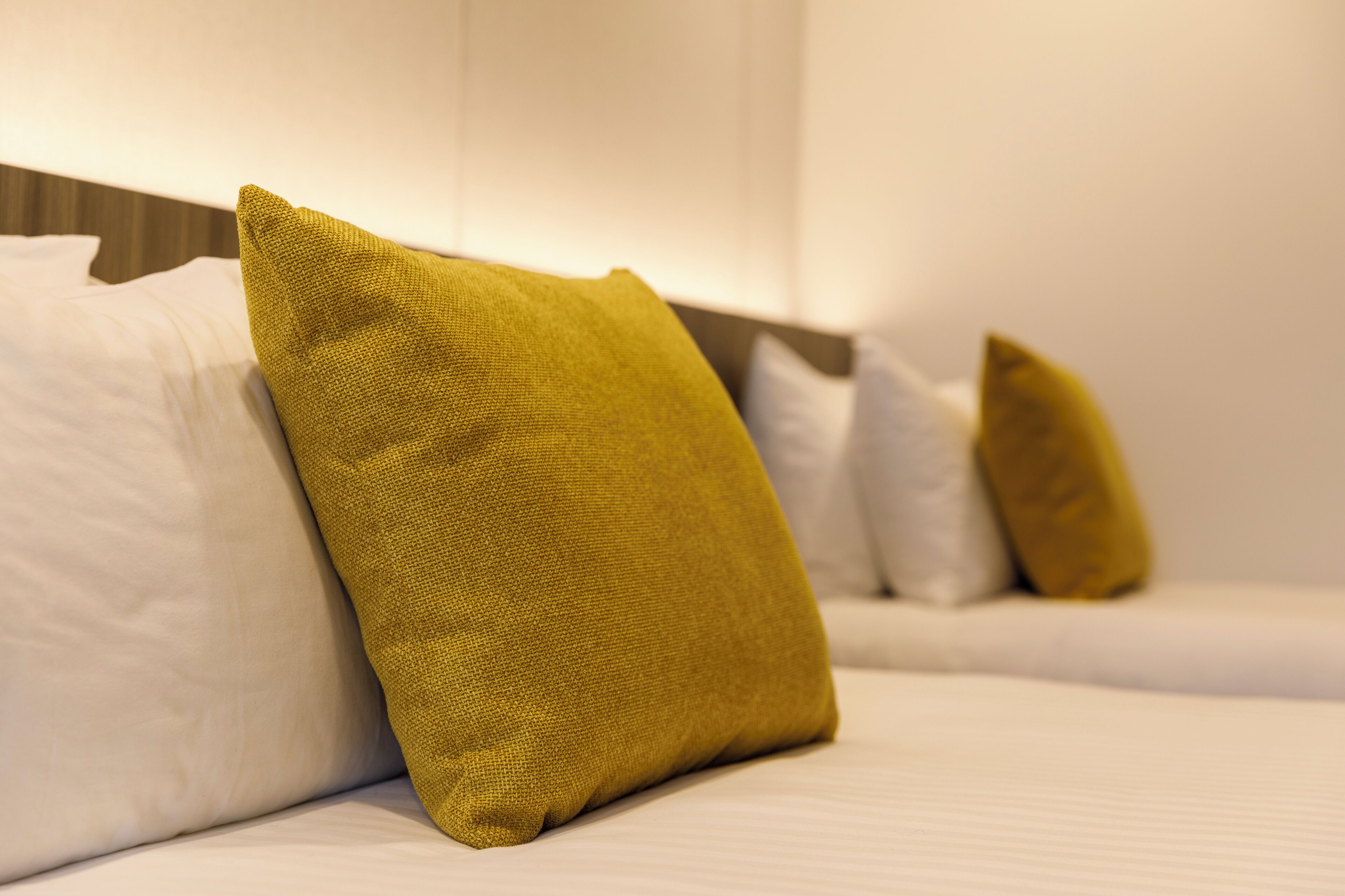 A neatly made bed with white and mustard yellow pillows.