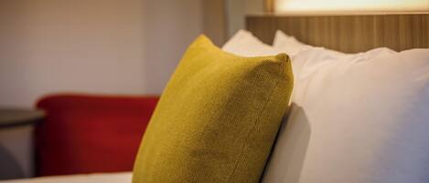 Una habitación de hotel con una cama bien hecha, una silla roja y una lámpara en la mesita de noche.