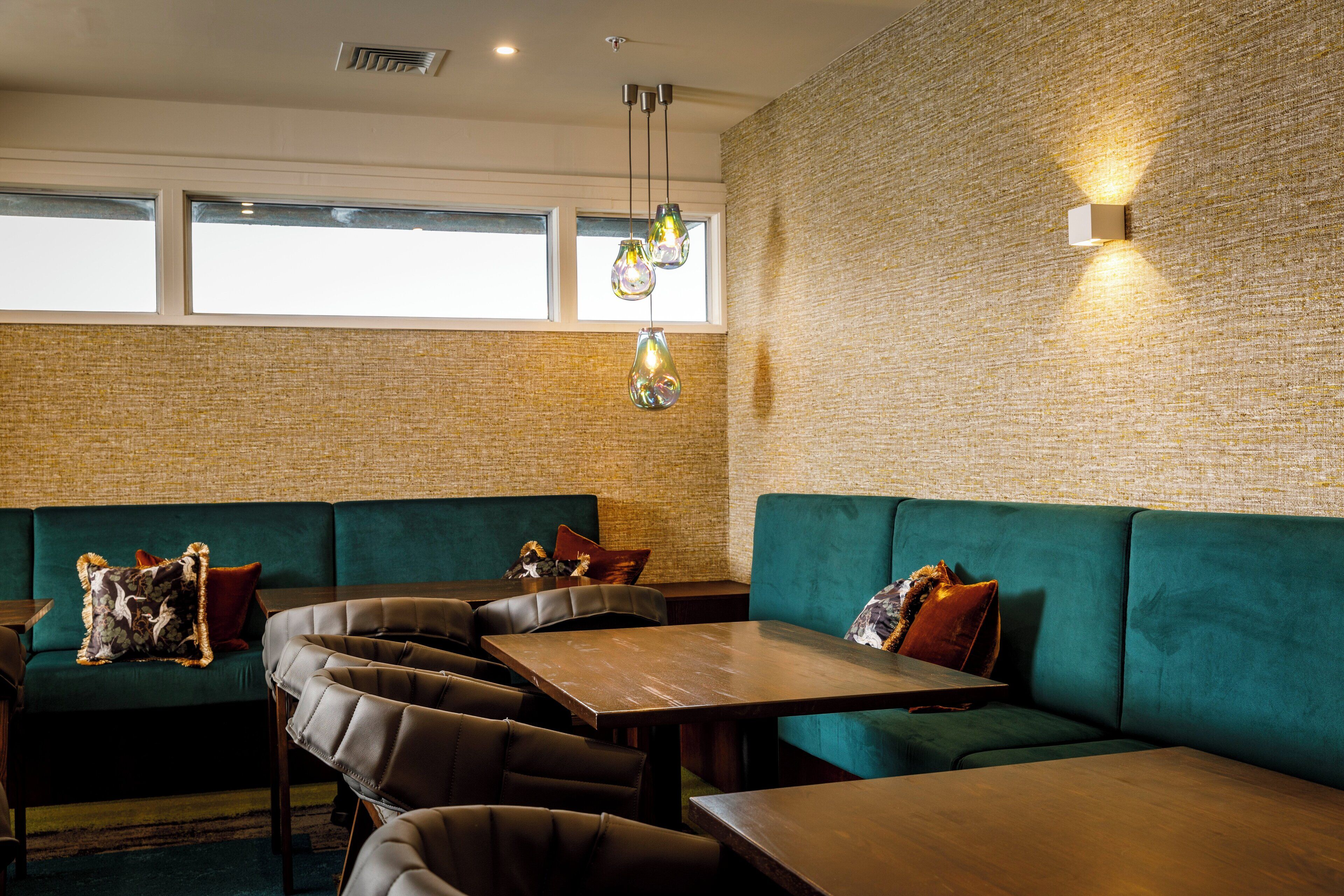 A restaurant with green upholstered booths, wooden tables, and hanging pendant lights.