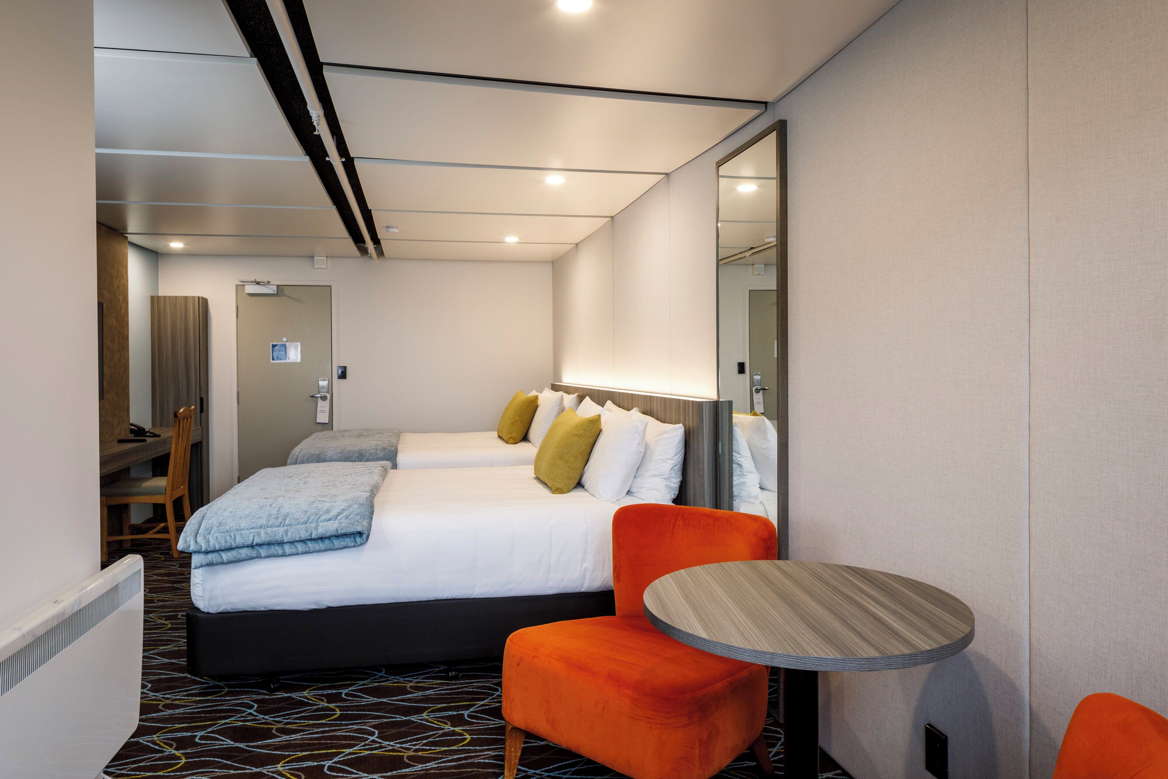 A hotel room with a bed, two chairs, a small table, and a mirror.