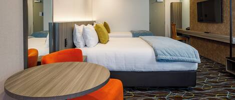 Habitación de hotel con una cama, dos sillones naranjas, una mesa redonda, un televisor y una alfombra estampada.