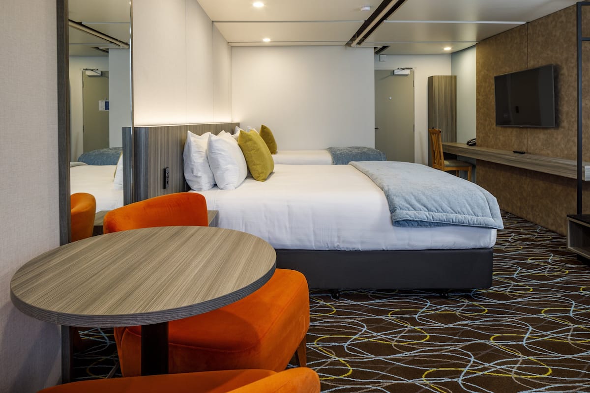 A hotel room with two beds, a desk, a chair, a TV, and a patterned carpet.