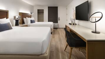 A hotel room with two beds, a desk, a chair, a TV, and a mirror.