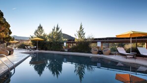 A clear swimming pool with lounge chairs and umbrellas, surrounded by trees and a building with a covered patio. - Sky Rock Sedona, a Tribute Portfolio Hotel (Sedona)