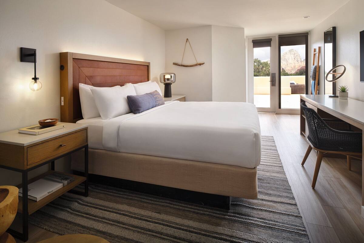 A modern bedroom with a large bed, bedside tables, a desk, and a view of the outdoors.