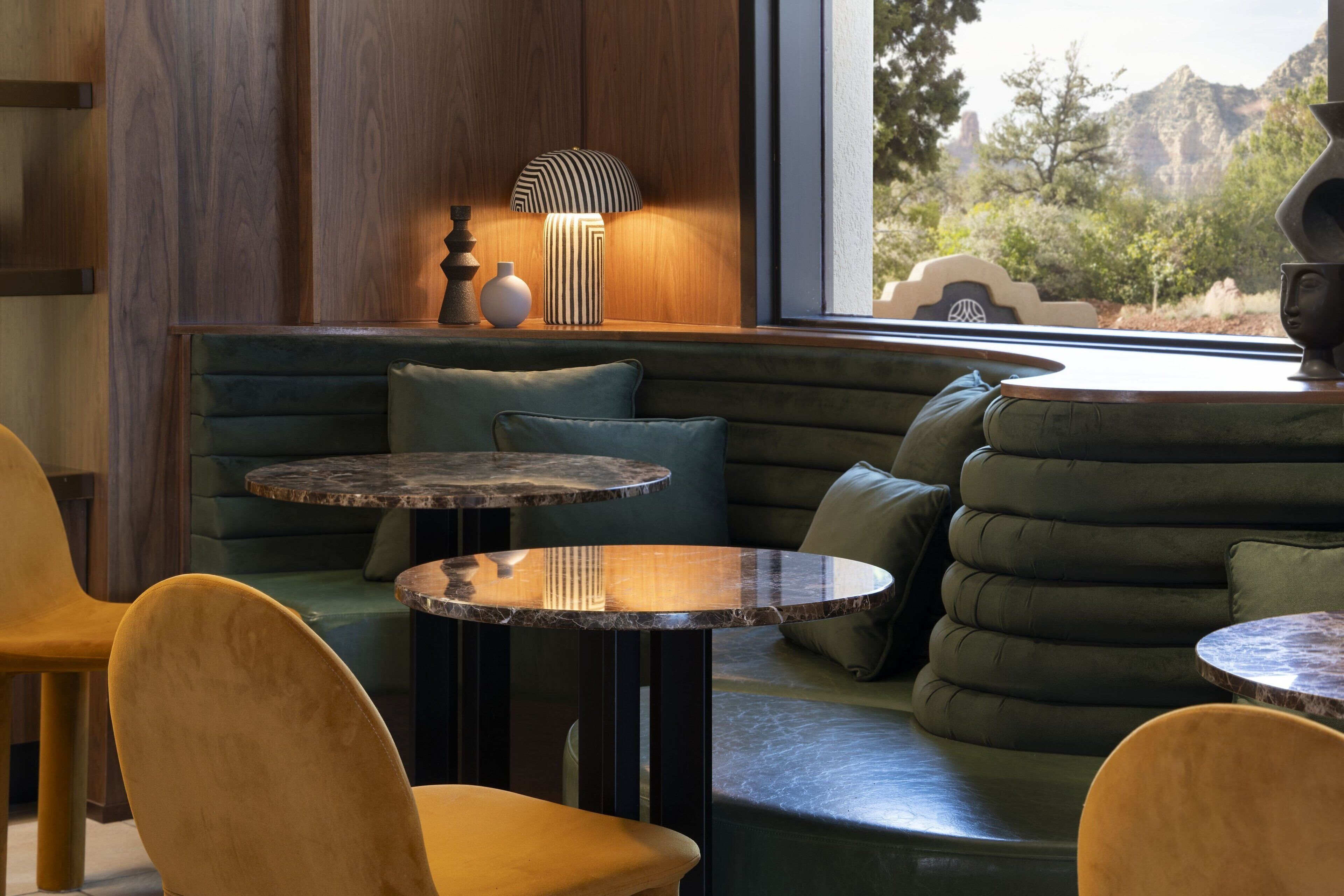 A cozy seating area with a cushioned bench, two round tables, and a lamp.