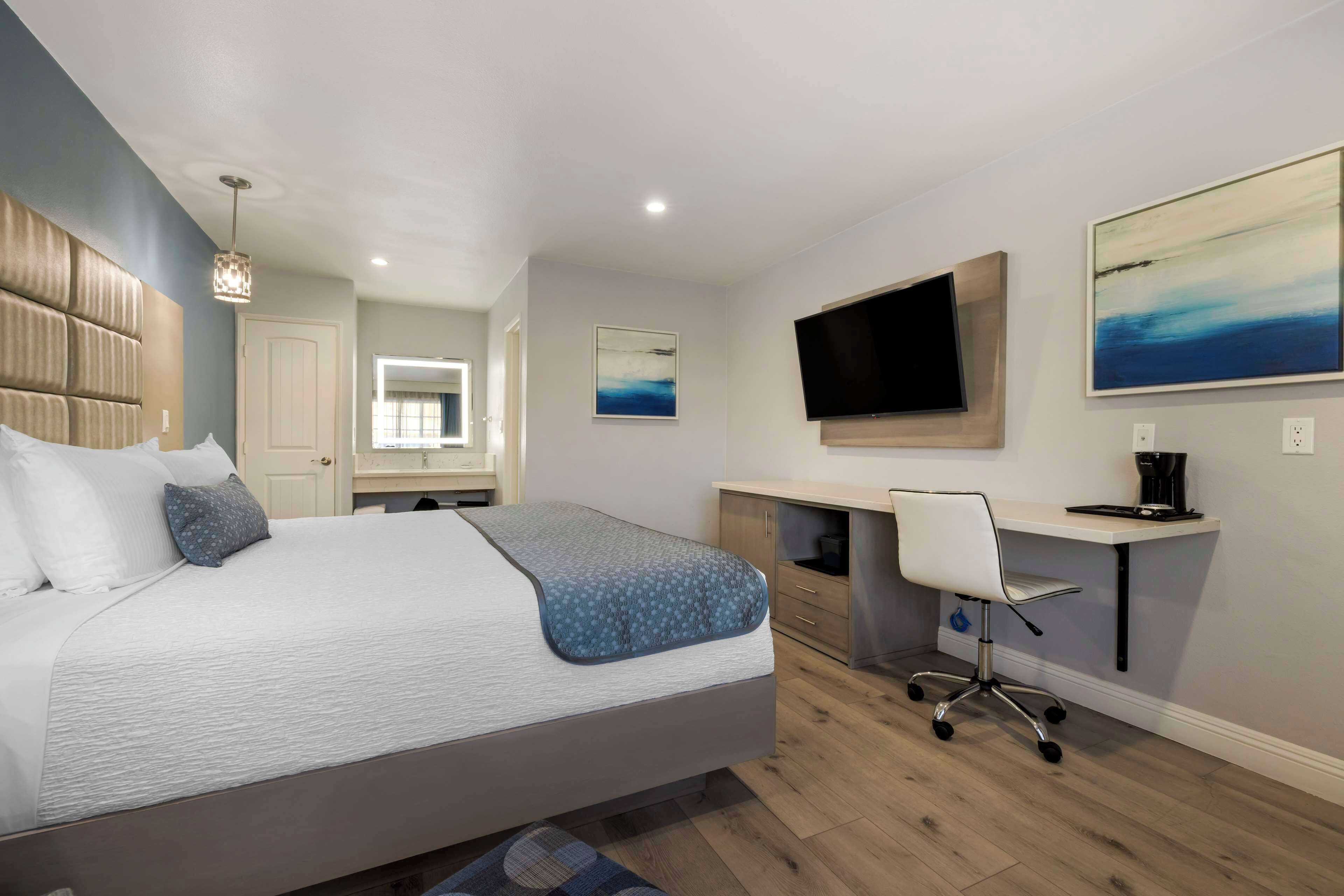 Ein modernes Schlafzimmer mit einem großen Bett, einem Schreibtisch, einem Sessel, einem Fernseher und Kunstwerken an den Wänden.