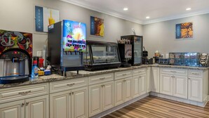 A modern kitchen with a coffee station, a juice dispenser, and a refrigerated display case. - Best Western Orange Plaza (Orange)