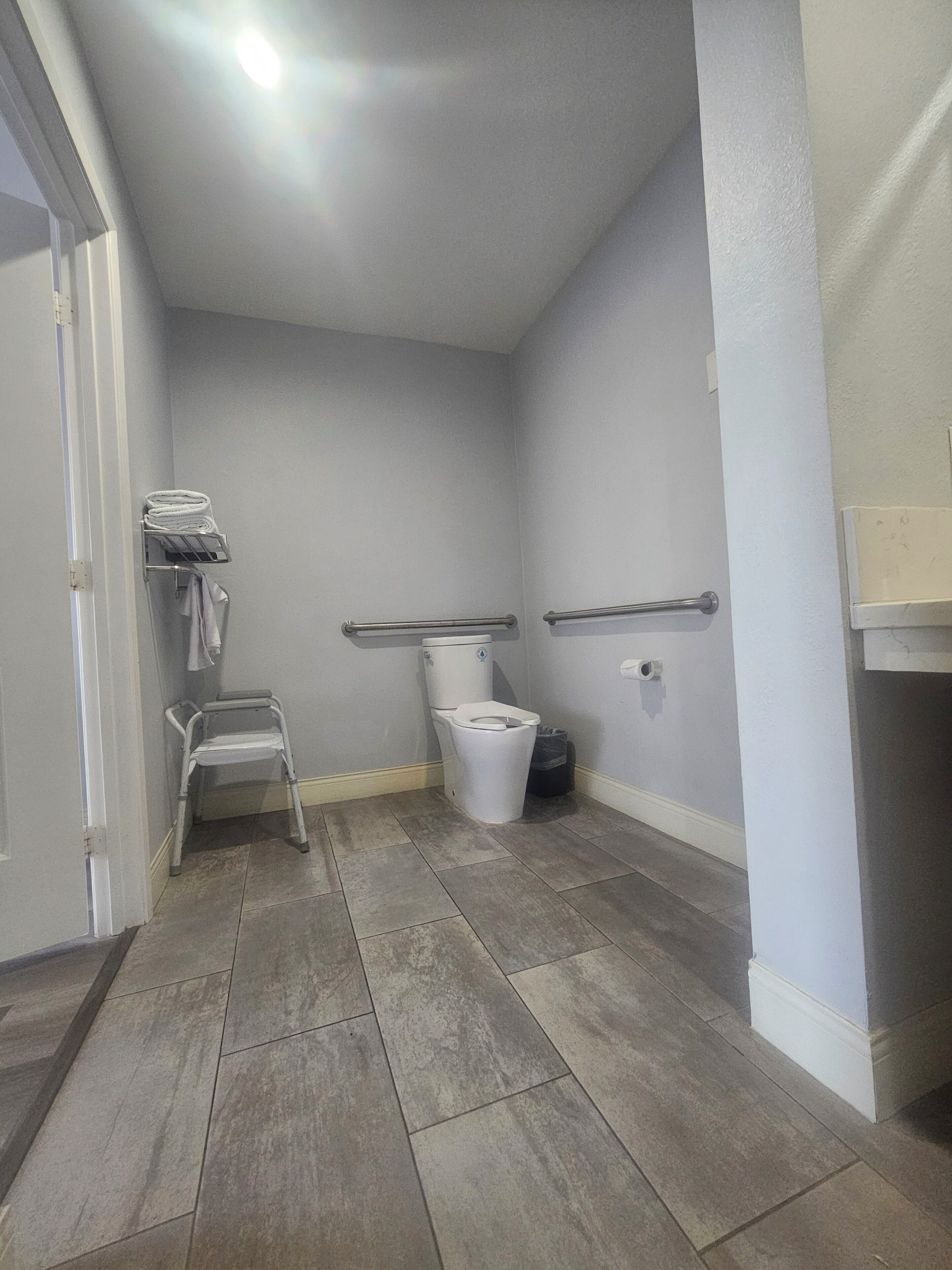 A bathroom with a toilet, a handrail, a towel rack, and a walker.
