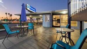 An outdoor patio area with tables and chairs, a Best Western sign, and a view of the street at dusk. - Best Western Orange Plaza (Orange)