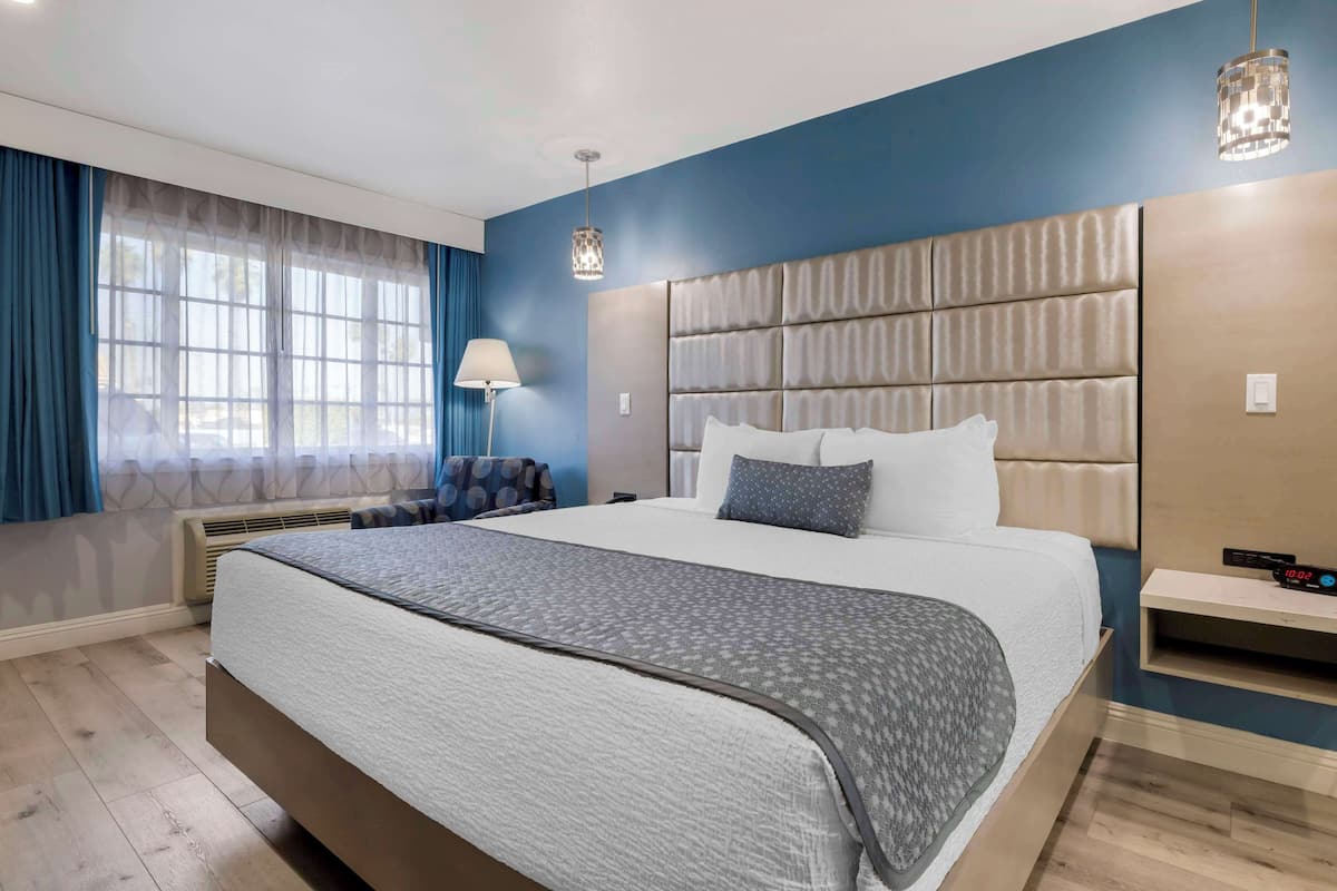 Une chambre d’hôtel moderne avec un grand lit, une table de chevet, une lampe et une vue sur l’extérieur par la fenêtre.