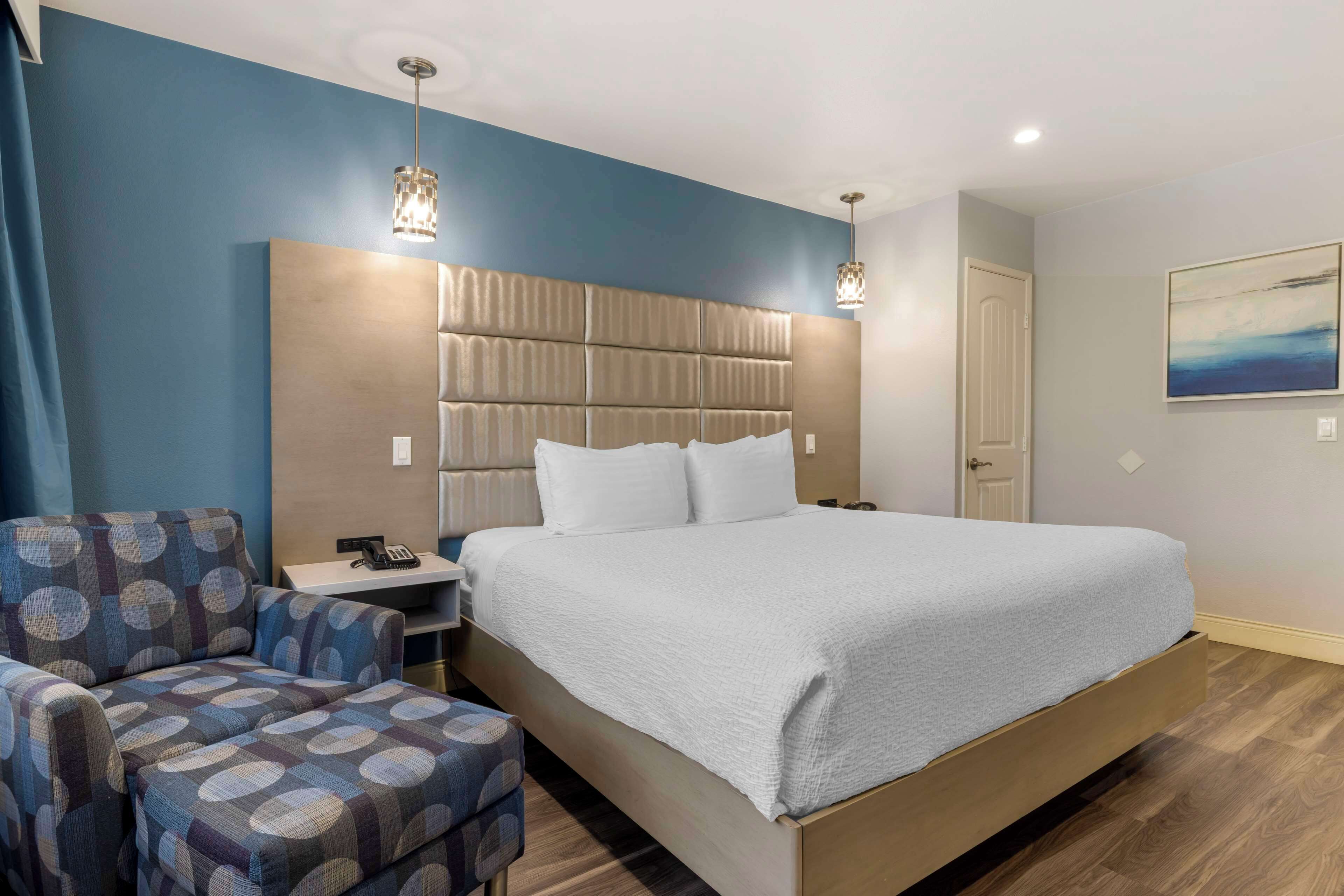 Una habitación de hotel moderna con una cama grande, una mesita de noche, una silla y un cuadro en la pared.