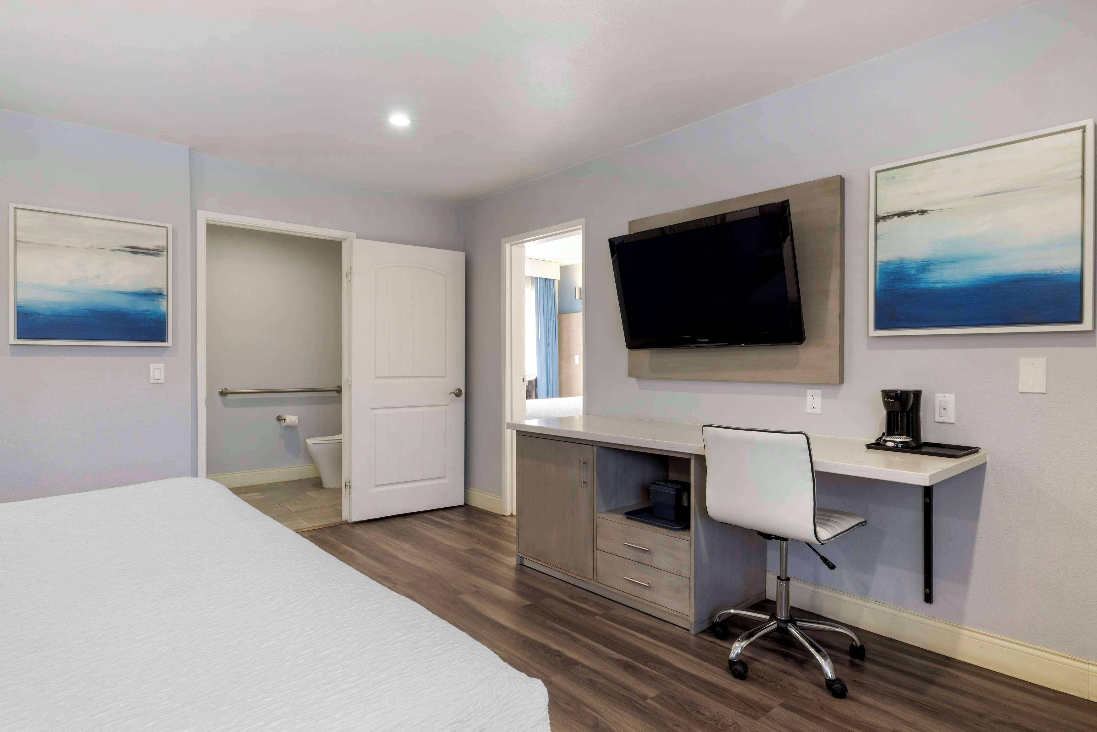 A hotel room with a bed, a desk with a chair, a television, and artwork on the walls.