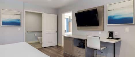 A hotel room with a bed, a desk with a chair, a television, and artwork on the walls.
