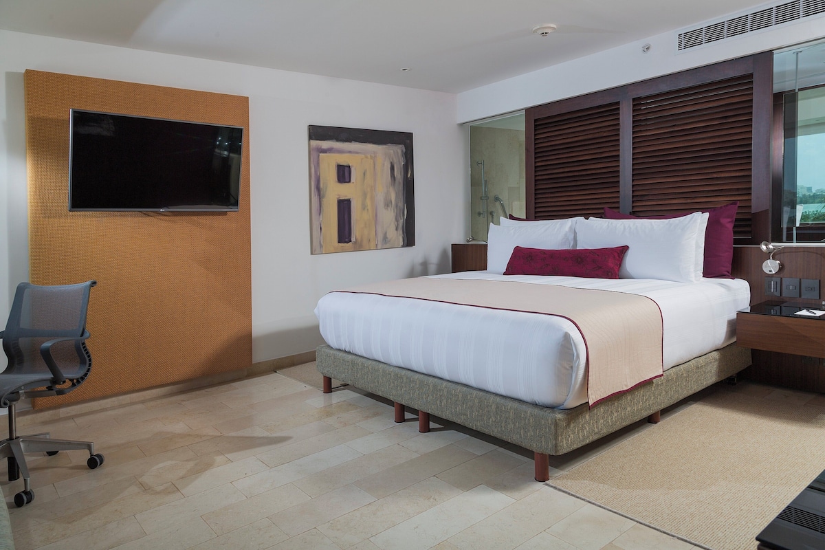 A modern hotel room with a large bed, a desk, a chair, and a television mounted on the wall.
