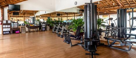 A spacious gym with wooden floors, exercise equipment, and potted plants.