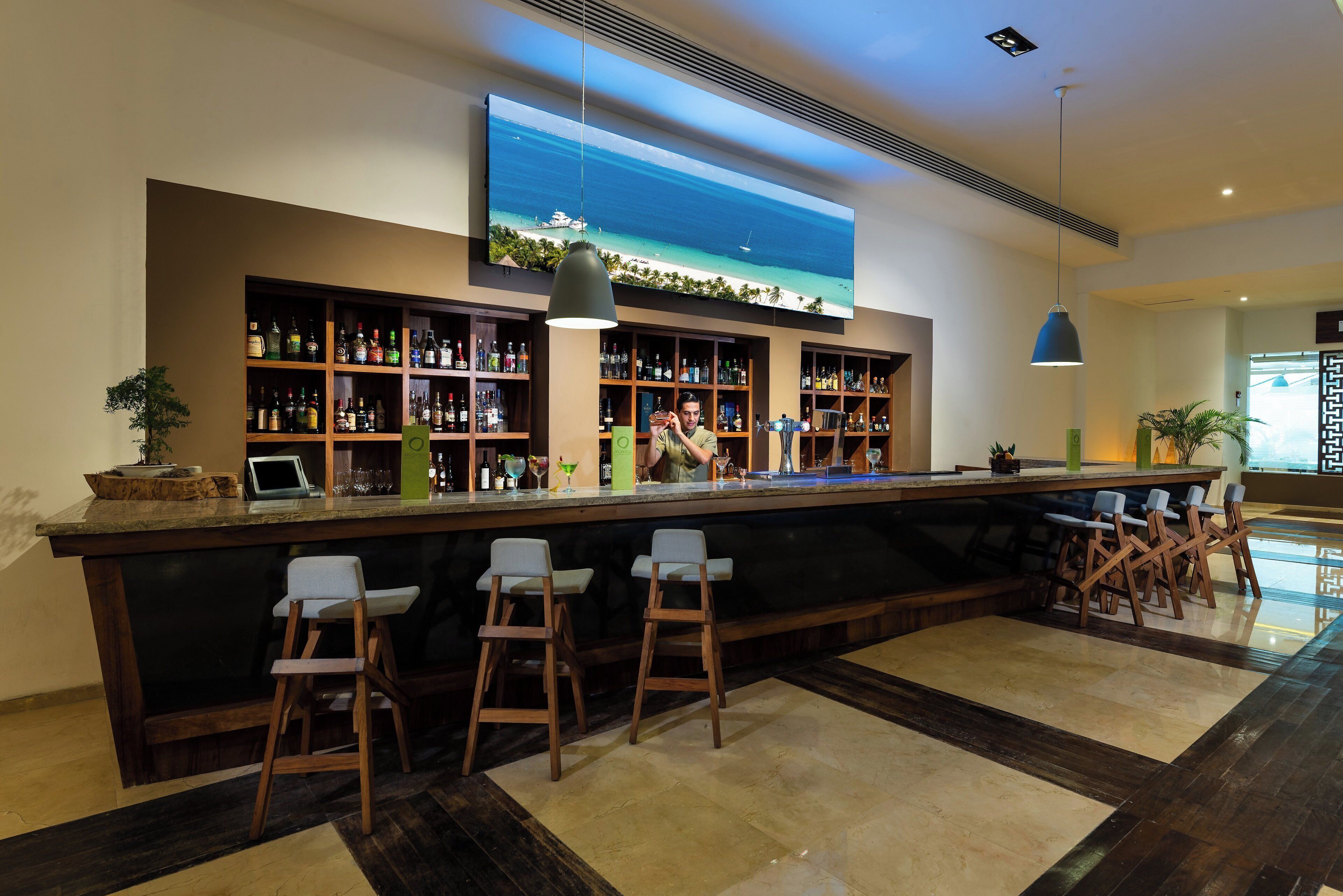 Zona de bar con una barra larga, varias estanterías llenas de botellas y taburetes.
