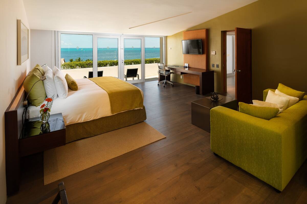 A hotel room with a bed, a desk, a green sofa, and a TV.