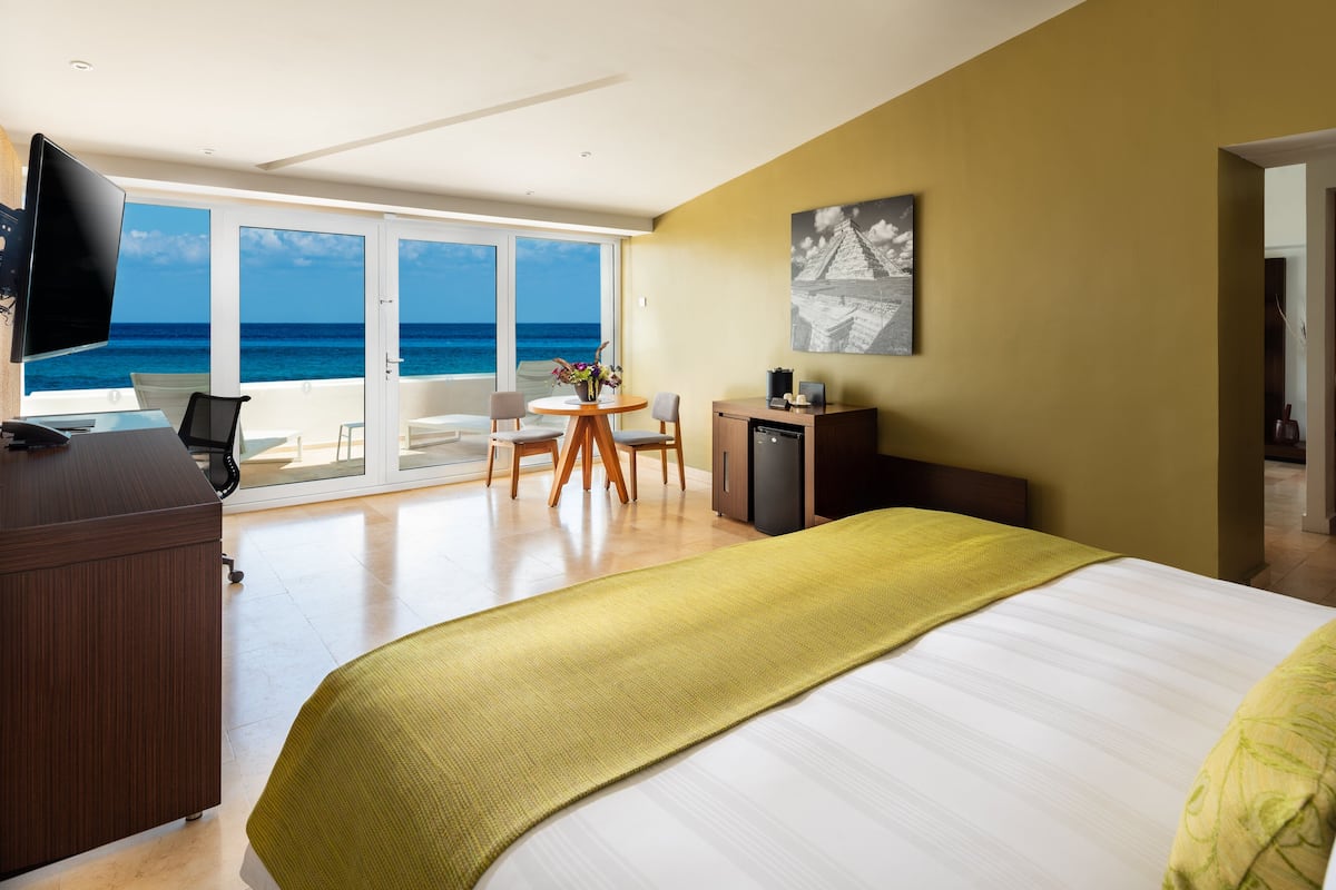 A hotel room with a bed, a desk, a chair, a television, and a view of the ocean.