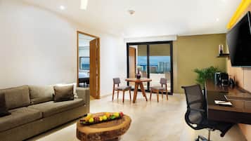 Una sala de estar moderna con un sofá, una mesa de comedor con sillas, una mesa de centro de madera con fruta y un televisor en la pared.
