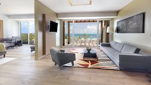 A modern living room with a grey sofa, a grey armchair, and a TV mounted on the wall. There is a balcony with a view of the ocean and palm trees. - InterContinental Presidente Cancun Resort by IHG (Cancun)