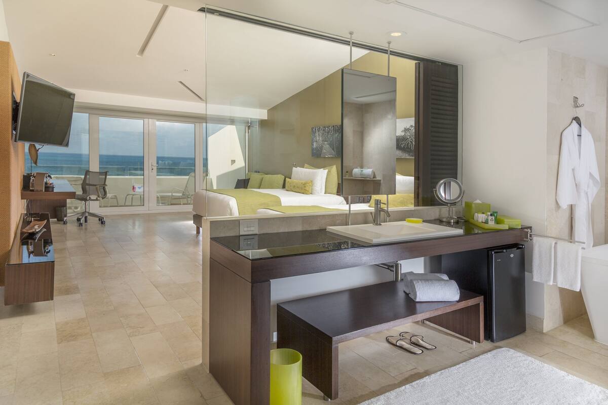 A modern hotel room with a large bed, a desk, a bathroom, and a view of the ocean.