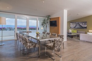 Una sala moderna con una mesa de comedor de vidrio, sillas con estampado floral, un sofá y un televisor montado en la pared.