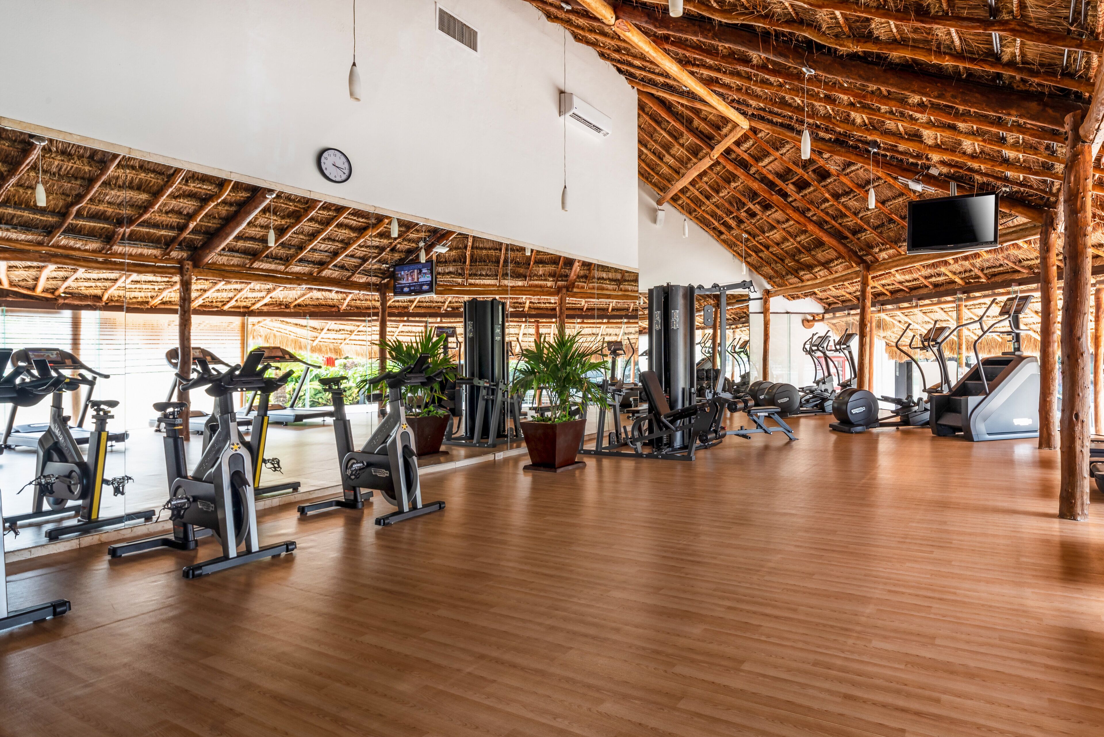 A spacious gym with wooden floors, exercise equipment, and a thatched roof.
