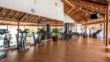 A spacious gym with wooden floors, exercise equipment, and a thatched roof.