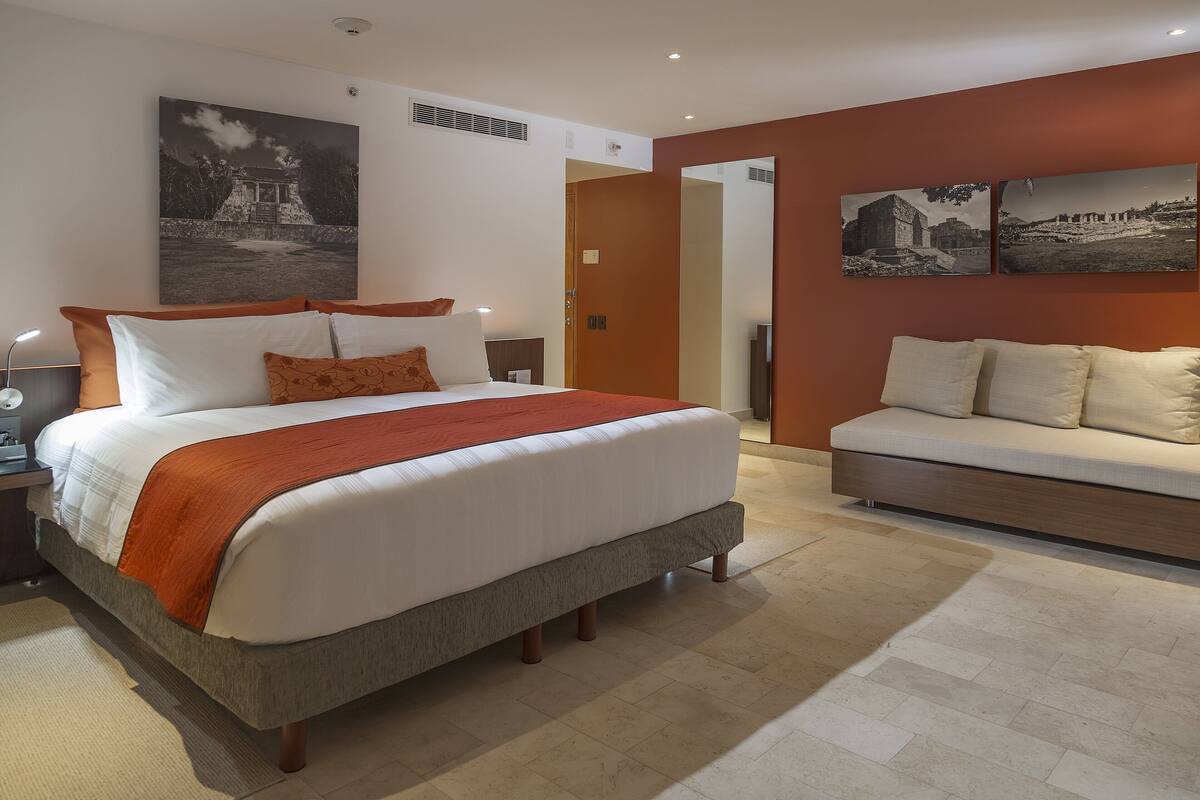 A modern bedroom with a large bed, a sofa, and two wall-mounted pictures.