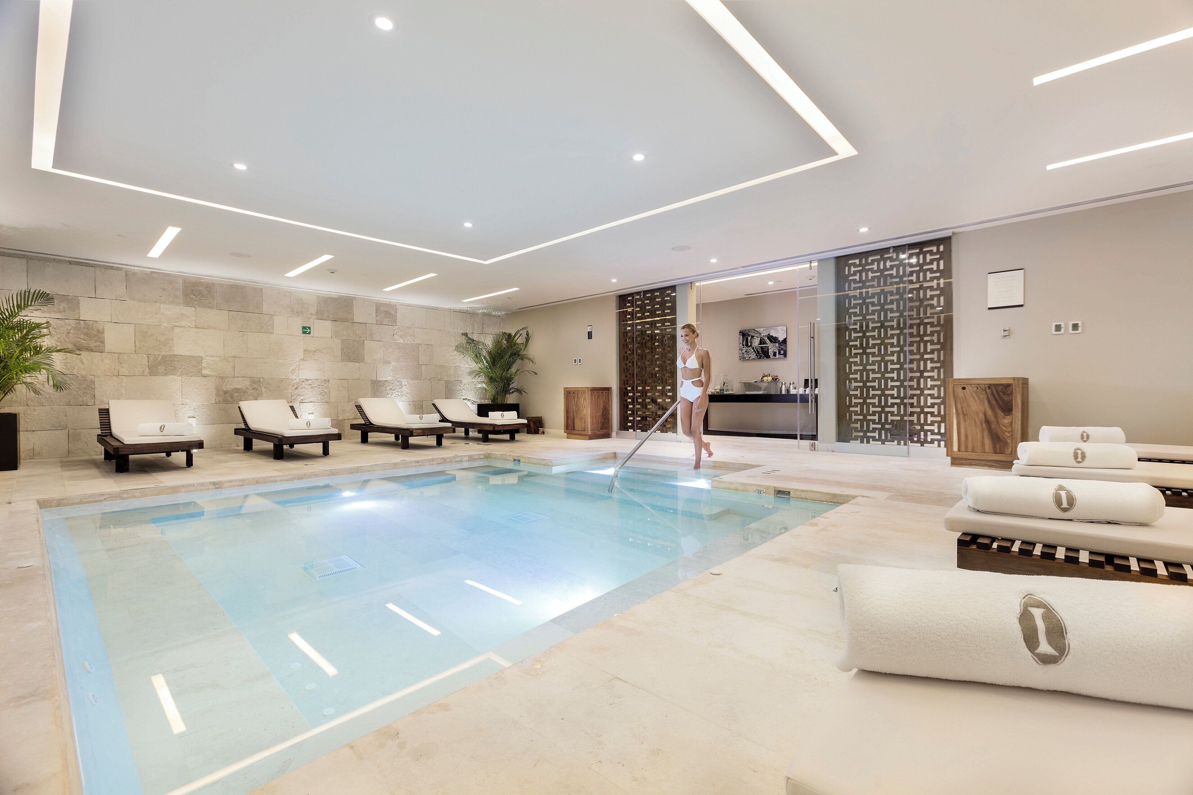Une piscine intérieure moderne, dotée de chaises longues et d’un espace dédié aux soins.