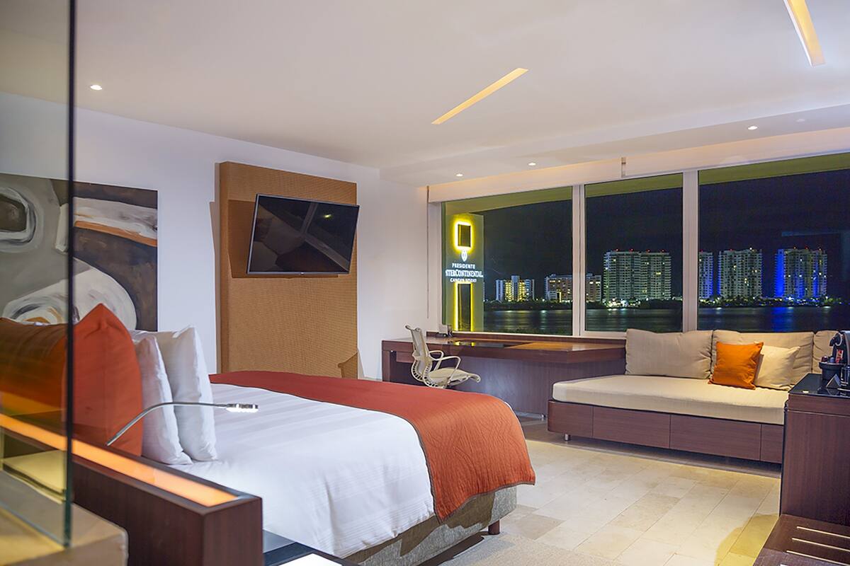 A hotel room with a bed, a sofa, a desk, and a large window with a city view.