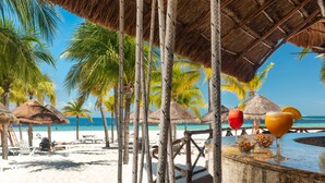 A wooden deck with rope swings, a bar area with a drink, and a beach with palm trees and a thatched roof structure. - InterContinental Presidente Cancun Resort by IHG (Cancun)