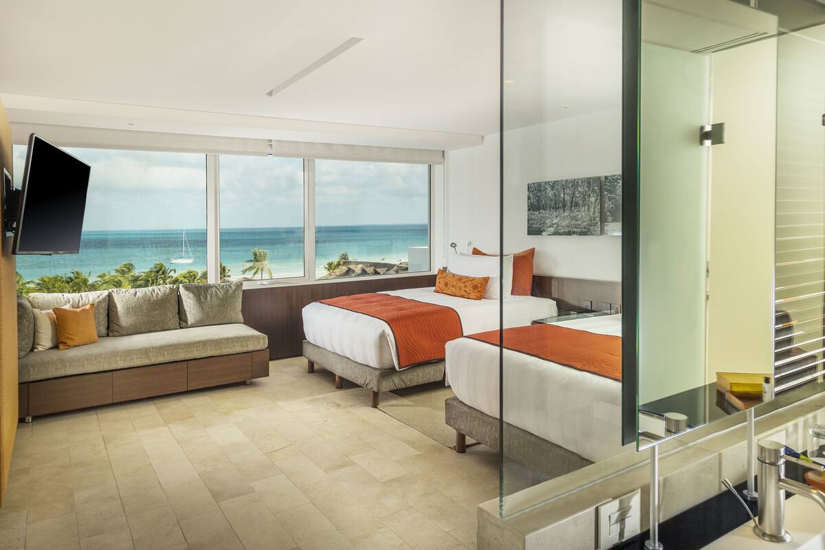 A hotel room with a large window, a sofa, two beds, and a TV.