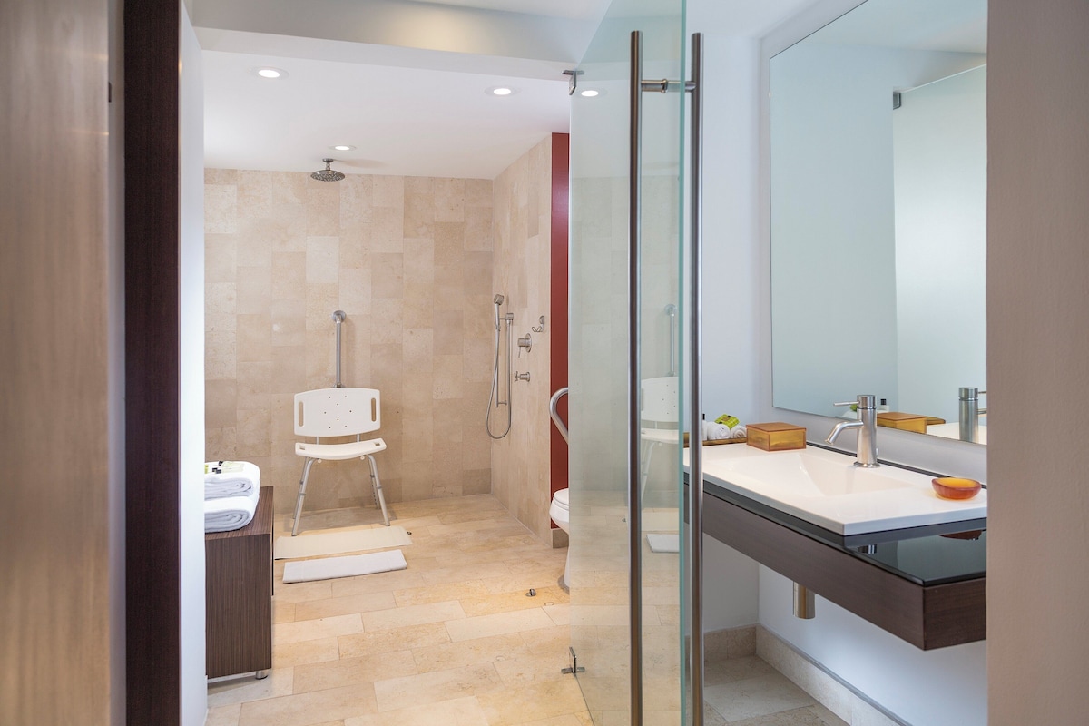 A modern bathroom with a glass shower enclosure, a white sink with a dark countertop, and a large mirror.
