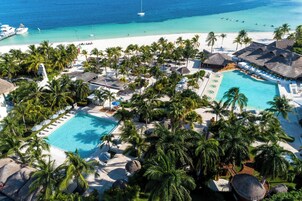 Un resort con dos piscinas, una playa y palmeras.