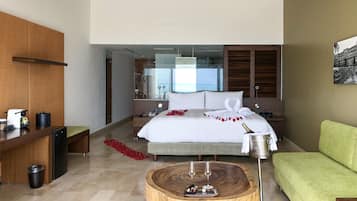 Habitación de hotel con cama, sofá verde, mesa de centro de madera con vasos, un cubo de basura y un mini bar.
